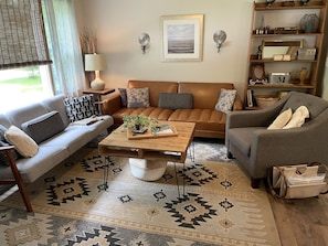 A living room with a brown leather sofa, grey armchairs, a wooden coffee table, and a patterned rug.