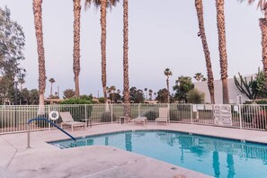 Una piscina con sillas de descanso y una valla, rodeada de altas palmeras.