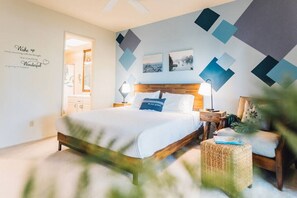 Un dormitorio con cama, mesita de noche, lámpara y pared decorada con patrones geométricos y una cita motivacional.