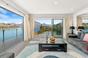 A modern living room with a large glass door leading to a balcony with a lake view.