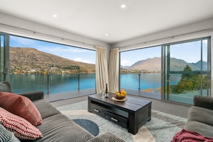 A modern living room with a large window overlooking a lake and mountains.
