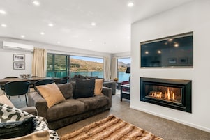 A modern living room with a fireplace, comfortable seating, and a scenic view of a lake.
