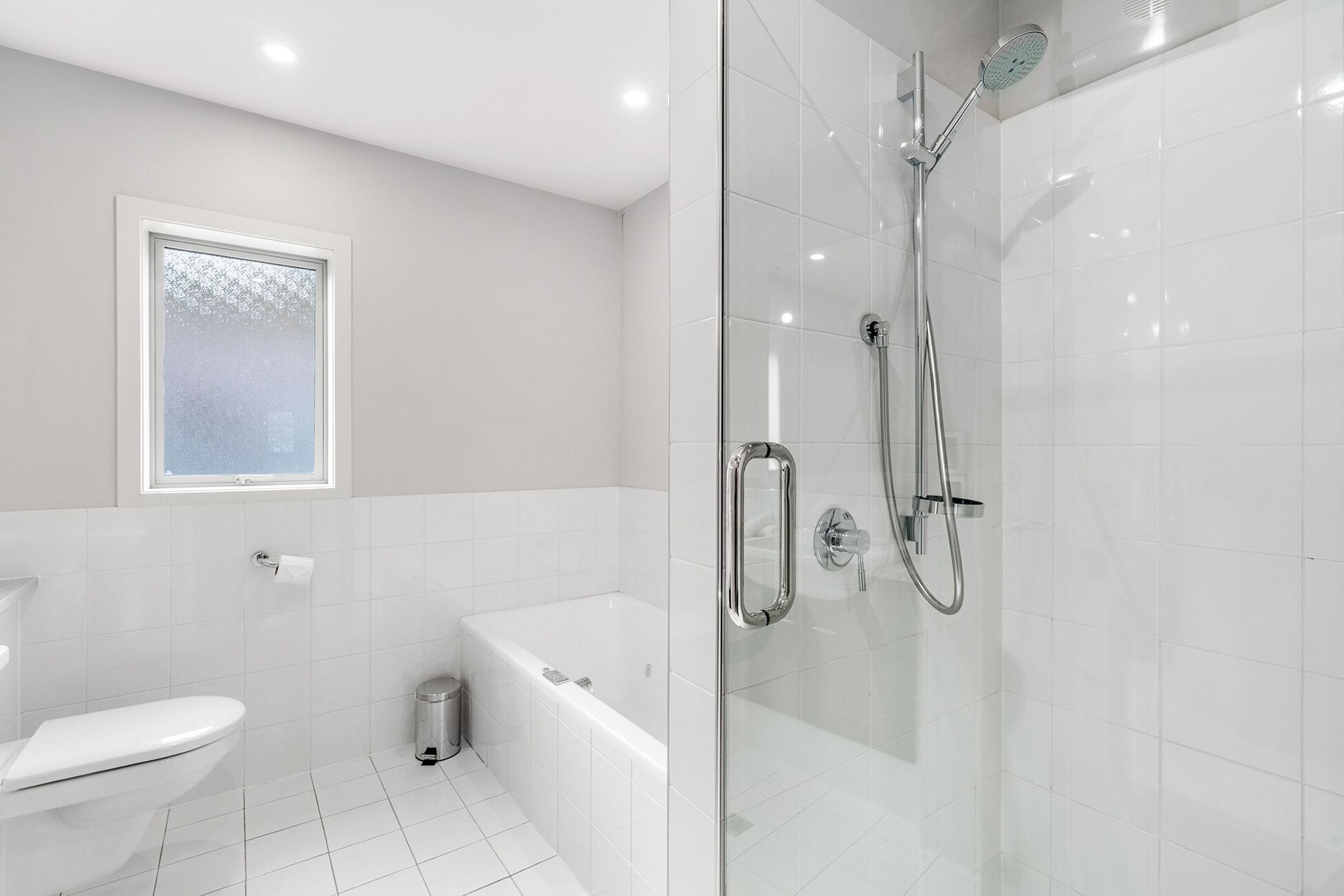 Een moderne badkamer met een douchecabine, een wit toilet en een bad.