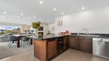 A modern kitchen with a central island, dark wooden cabinets, stainless steel appliances, and a dining area with a view of mountains.