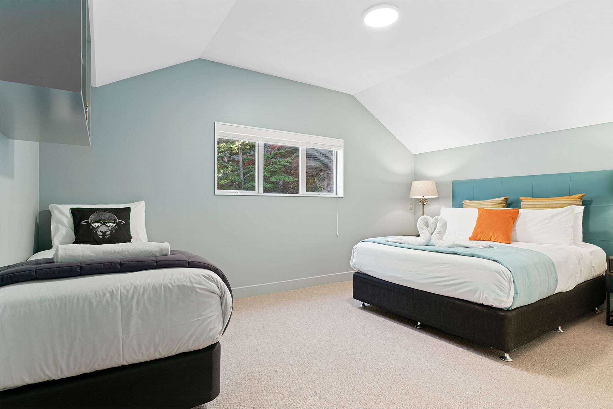 Une chambre avec deux lits, une fenêtre donnant sur des arbres et un luminaire au plafond.