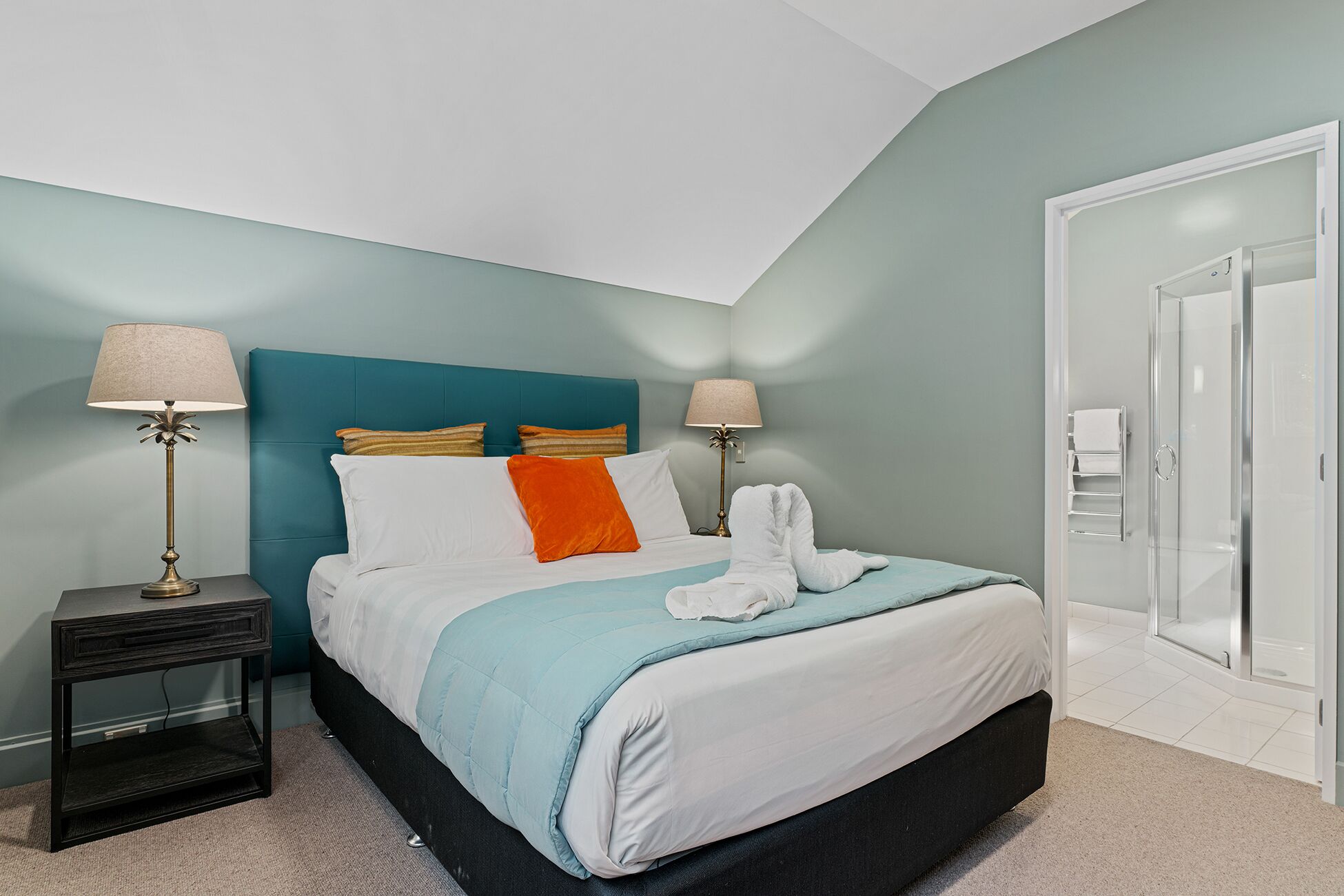 A modern bedroom with a bed, two bedside tables, a nightstand, a shower, and a door.