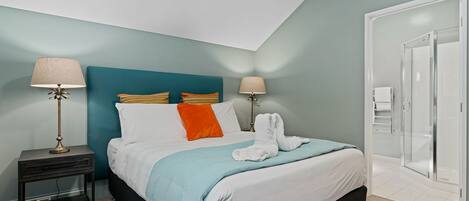 A modern bedroom with a bed, two bedside tables, a nightstand, a shower, and a door.