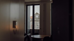 A room with a large window, a clock, and a view of a building with a clock tower. - Courtyard Oporto Design Apartment D (Porto)