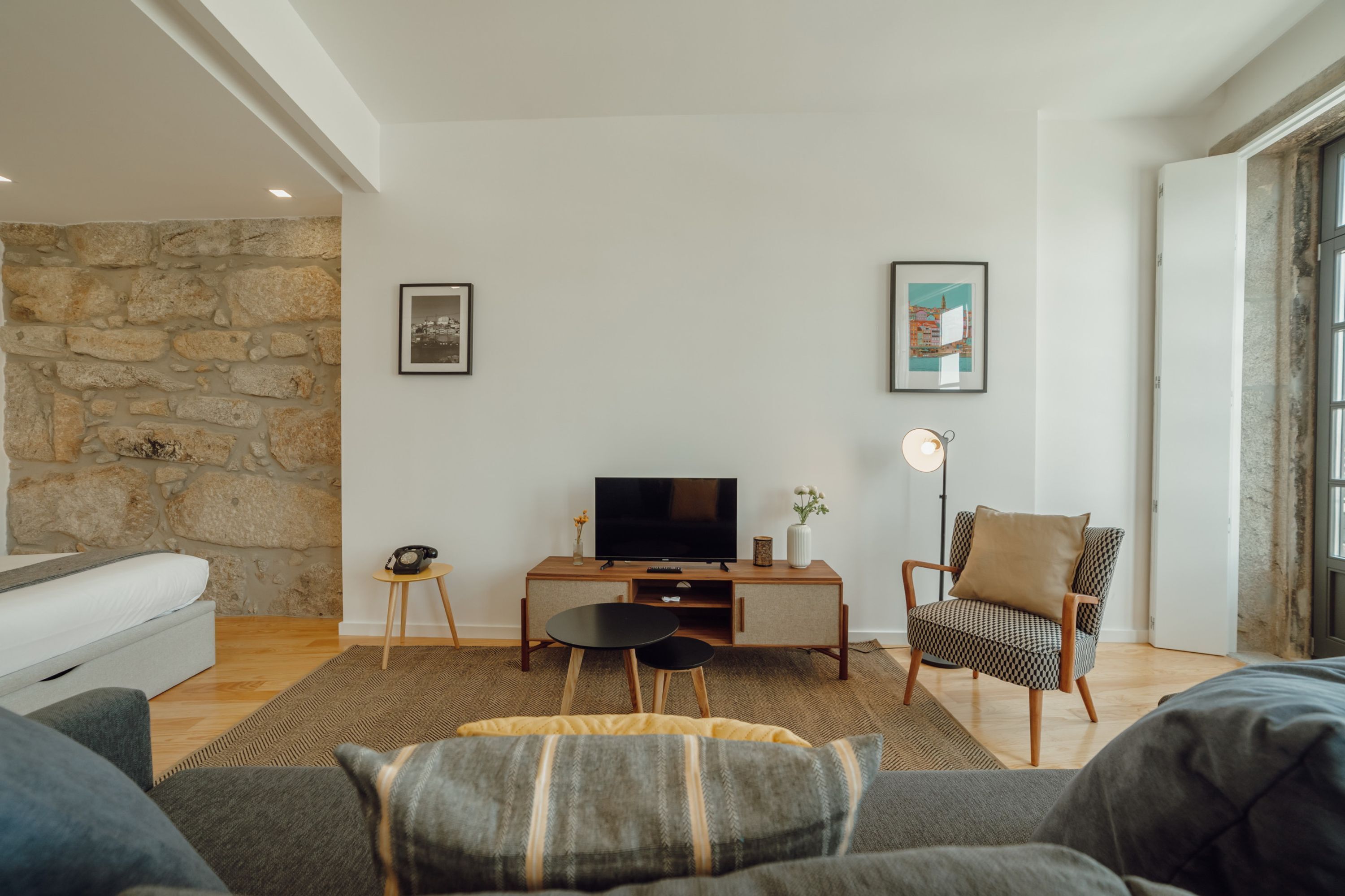 Uma sala de estar moderna com parede de pedra, televisão de tela plana, sofá, poltrona e uma pequena mesa lateral.