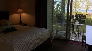 A hotel room with a bed, a nightstand with a lamp, a sliding glass door leading to an outdoor patio with chairs and a table.