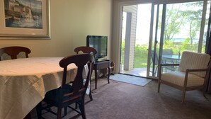 A dining area with a table, chairs, a television, and a view through a sliding glass door.