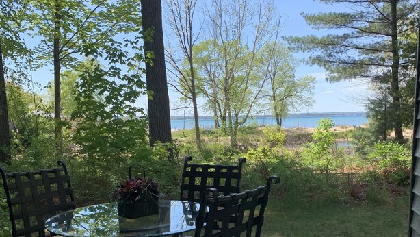 A deck with a glass-top table and four chairs, overlooking a grassy area and a body of water.