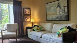 A room with a white sofa, a wooden chair, a lamp, and two framed pictures on the wall.