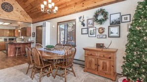A dining area with a wooden table and chairs, a chandelier, and a Christmas tree. - Christmas Cottage - Cozy cabin in the Pines! (Pinetop)