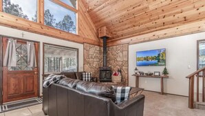 A cozy living room with a stone fireplace, a large window, and a wooden ceiling. - Christmas Cottage - Cozy cabin in the Pines! (Pinetop)