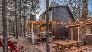 A cabin with a deck, picnic table, and string lights. - Christmas Cottage - Cozy cabin in the Pines! (Pinetop)