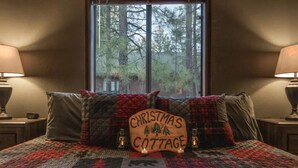 A cozy bedroom with a bed, a Christmas cottage sign, and a window view. - Christmas Cottage - Cozy cabin in the Pines! (Pinetop)