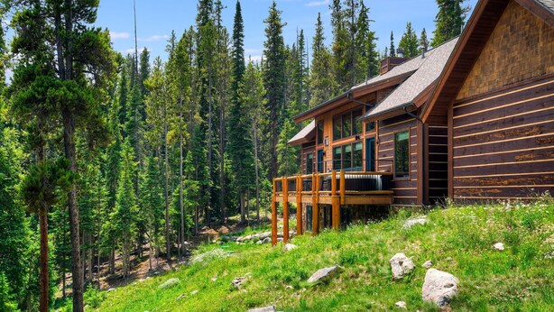 Eine Blockhütte mit einer Terrasse, umgeben von einem Wald.