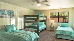 Une chambre avec des lits superposés, deux lits simples, un ventilateur de plafond et une fenêtre donnant sur un beau paysage.