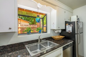 Eine Küche mit einem doppelten Waschbecken, einem Kühlschrank und einem Fenster mit einem hängenden Ziergegenstand.