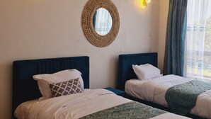 Une chambre d’hôtel avec deux lits, un miroir rond et deux lampes fixées au mur.