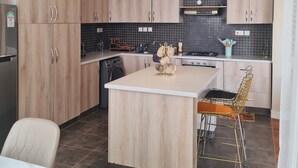 Une cuisine moderne avec des meubles en bois, un îlot central et un coin repas équipé d’une chaise.