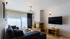 A modern living room with a dark sofa, a flat-screen TV, a fireplace, and a large window with sheer curtains. - Villa Melki SAVE 20 percent on Split-villas com (Klis)