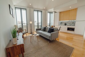A modern living room with a grey sofa, a coffee table, and a wooden sideboard. There is a large window with a view of buildings outside. - Courtyard Oporto Design Apartment F (Porto)