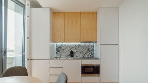 Una cocina moderna con armarios blancos, un gabinete superior de madera, salpicadero de mármol, una cafetera negra y un horno empotrado.