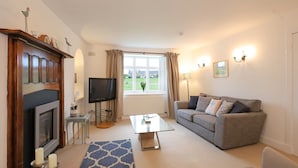 A living room with a fireplace, television, sofa, and a view of the outdoors. - Two bed period cottage in Gullane sleeping up to 4 guests. (Gullane)