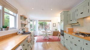 A kitchen with wooden countertops, light green cabinets, a dining area with a table and chairs, and a view of the garden through the windows. - Two bed period cottage in Gullane sleeping up to 4 guests. (Gullane)