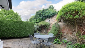 A patio with a round table and four chairs, surrounded by stone flooring and greenery. - Two bed period cottage in Gullane sleeping up to 4 guests. (Gullane)