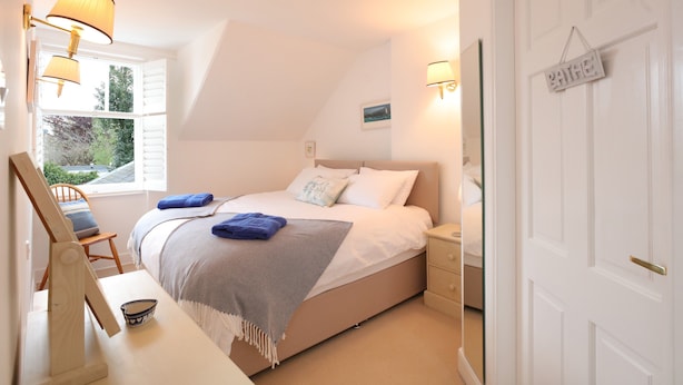 A bedroom with a bed, bedside tables, a desk with a chair, a window, and a door. - Two bed period cottage in Gullane sleeping up to 4 guests. (Gullane)