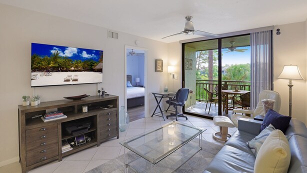 Ein modernes Wohnzimmer mit Flachbildfernseher, Glastisch, Sofa und einem Balkon mit Tisch und Stühlen.