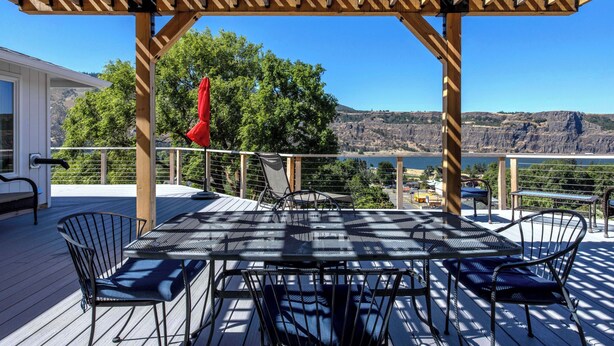 A covered outdoor deck with a table and chairs, overlooking a scenic landscape.