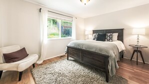A bedroom with a bed, bedside tables, a chair, a window with curtains, and a ceiling light.