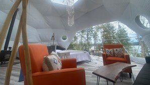 Un interior espacioso y de diseño único, con techo alto y ventanas amplias, que presenta asientos color naranja y una mesa central.
