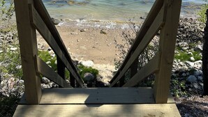 Una terraza de madera que da a una playa con agua cristalina y una orilla bordeada de bosque.