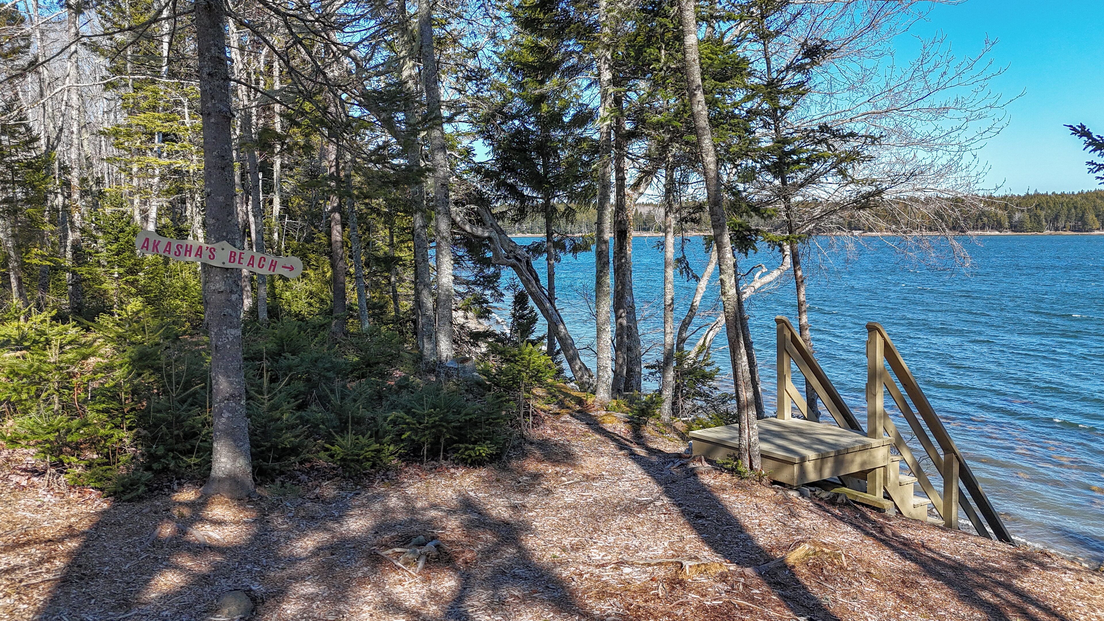 A wooden deck leading to a beach with a sign indicating 'Akasha's Beach'.