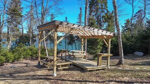 Un kiosque en bois, doté de tables de pique-nique et de bancs, entouré d’arbres et bordé par un plan d’eau.