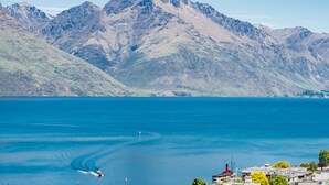 A mountainous landscape with a clear blue lake, a boat in the water, and buildings in the foreground. - TOWN CENTRE LOCATION WITH STUNNING VIEW - UNIT 1 (Queenstown)