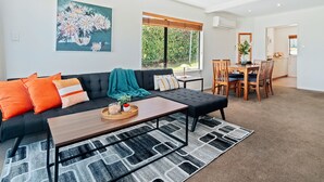A modern living room with a dark sofa, a coffee table, and a dining area with wooden chairs and a table. - TOWN CENTRE LOCATION WITH STUNNING VIEW - UNIT 1 (Queenstown)