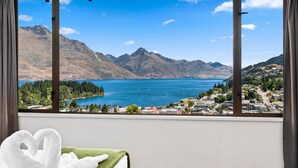 A room with a large window offering a view of a lake, mountains, and a town. - TOWN CENTRE LOCATION WITH STUNNING VIEW - UNIT 8 (Queenstown)