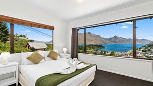 A hotel room with a large bed, a nightstand, a lamp, and a view of a lake and mountains. - TOWN CENTRE LOCATION WITH STUNNING VIEW - UNIT 8 (Queenstown)