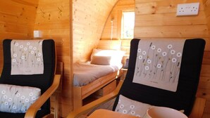 Tunnelmallinen mökin sisustus, jossa on puuseinät ja parvelle sijoitettu sänky. Siellä on kaksi tuolia, joissa on kukalliset koristetyynyt, sekä pöytä, jonka päällä on muki.
