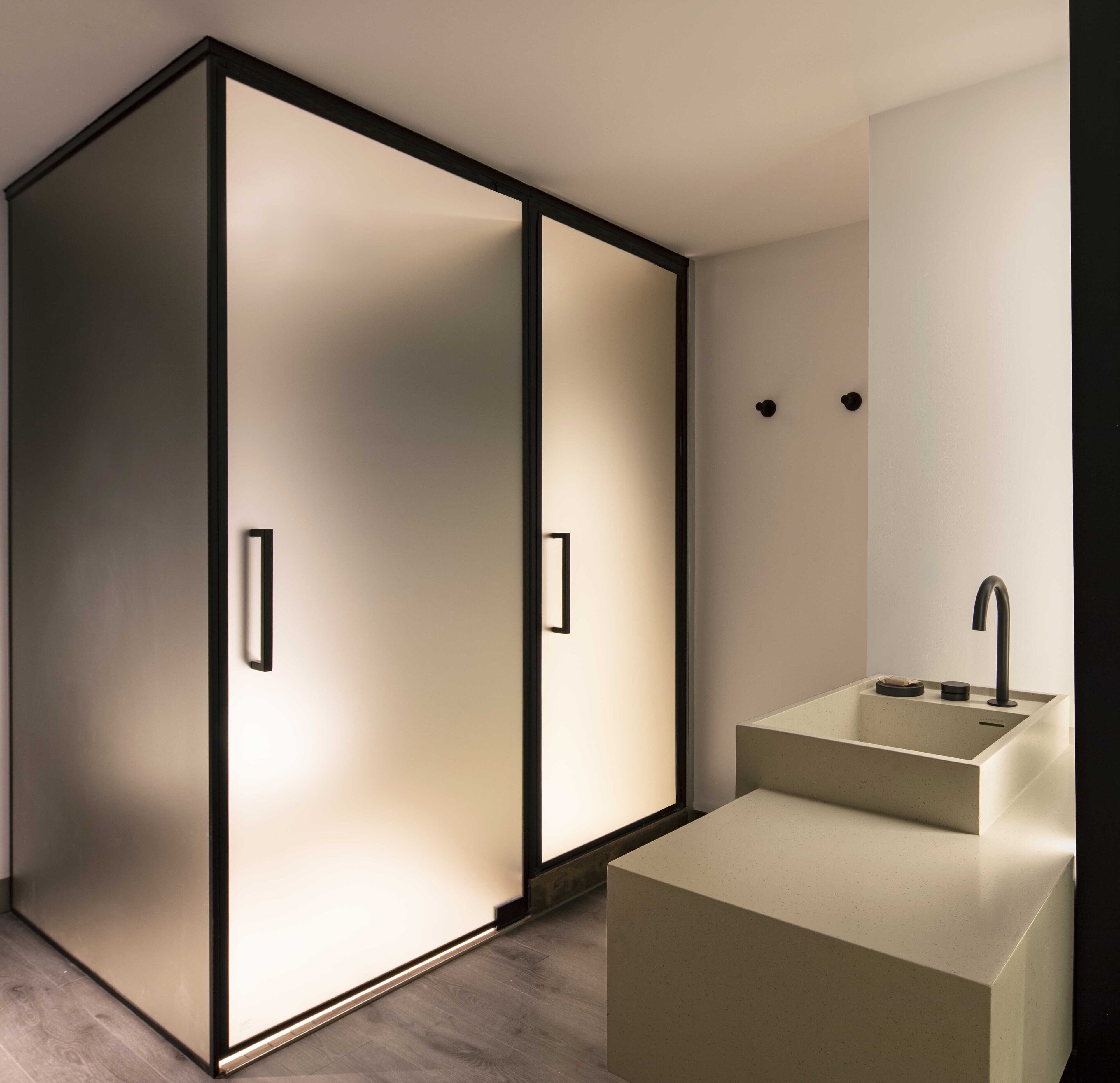 A modern bathroom with a minimalist design, featuring a large mirror, a sink, and a walk-in shower.