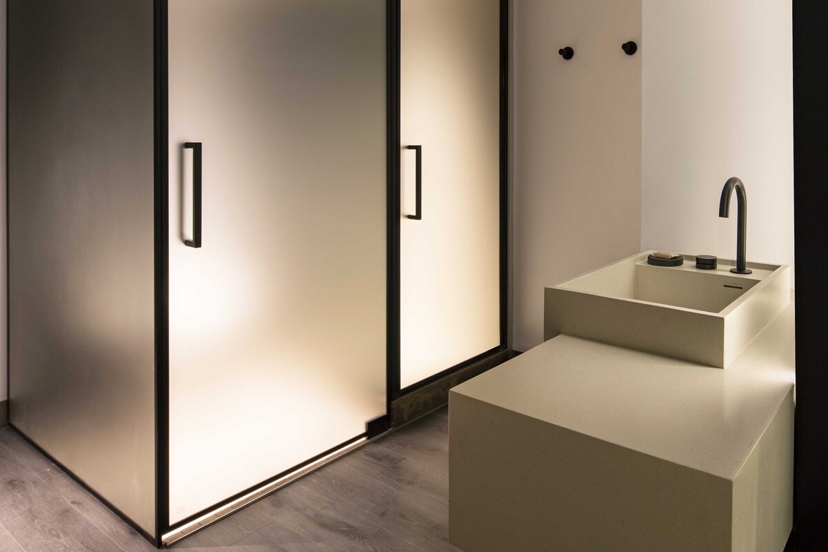 A modern bathroom with a minimalist design, featuring a large mirror, a sink, and a walk-in shower.