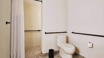 Un baño con inodoro, cortina de ducha, barra de apoyo y cubo de basura.