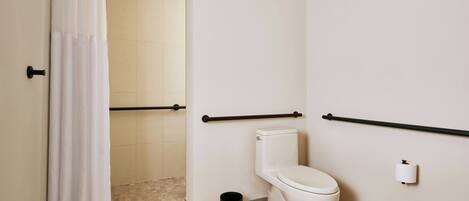 A bathroom with a toilet, a shower curtain, a grab bar, and a trash can.