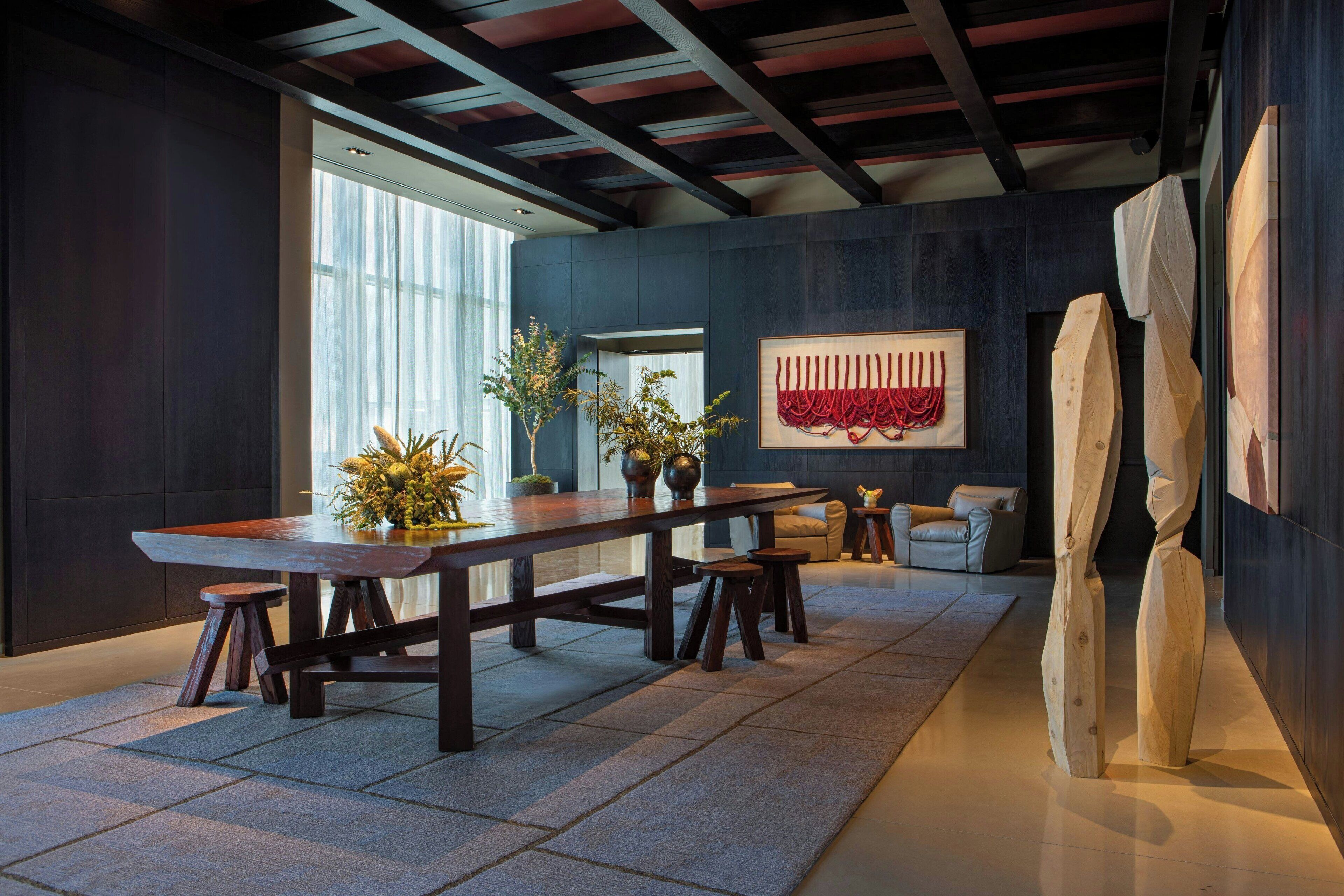A modern dining area with a long wooden table, stools, and potted plants.